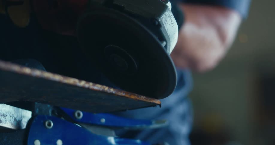 Slow-motion close-up of an angle grinder cutting a rusty metal sheet held in a vise, with sparks flying