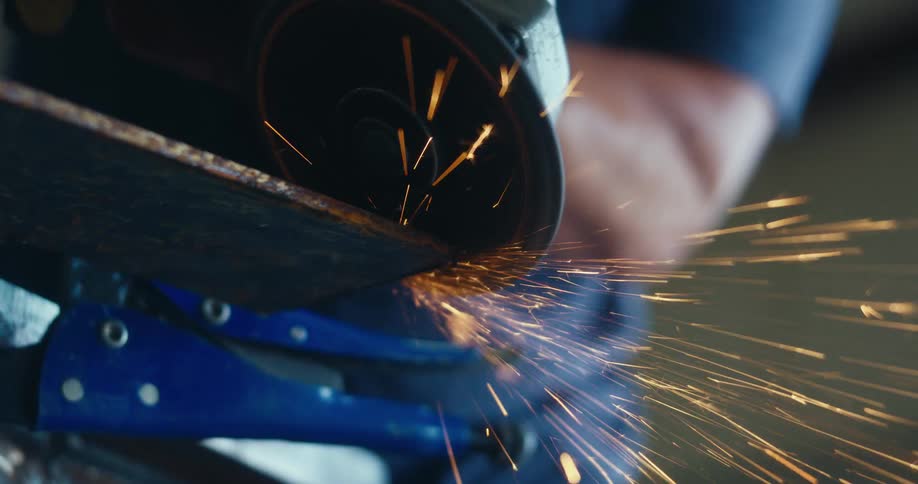 A close-up, slow-motion shot of an angle grinder cutting through rusty metal, sending a shower of bright orange sparks into the air