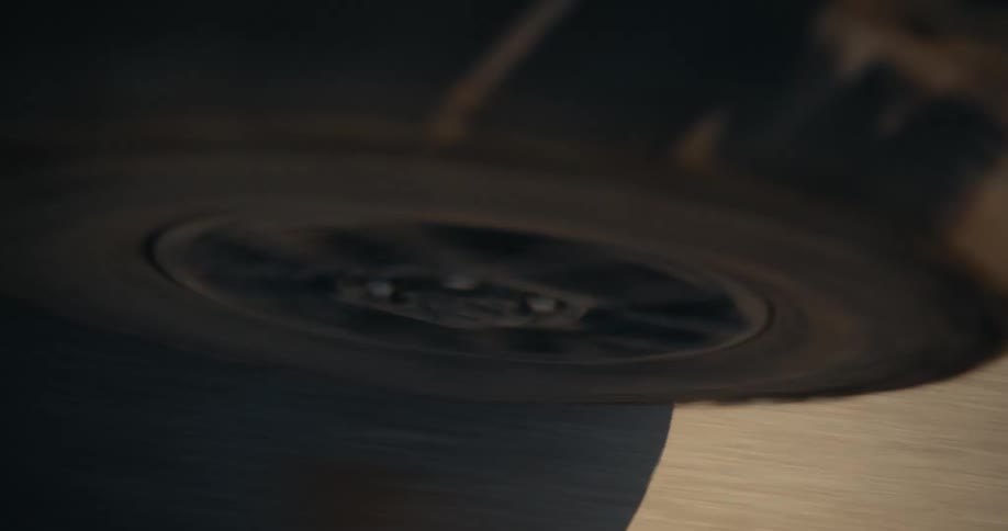 A top-down close-up shot of a dusty car tire spinning rapidly as it drives along a dirt road