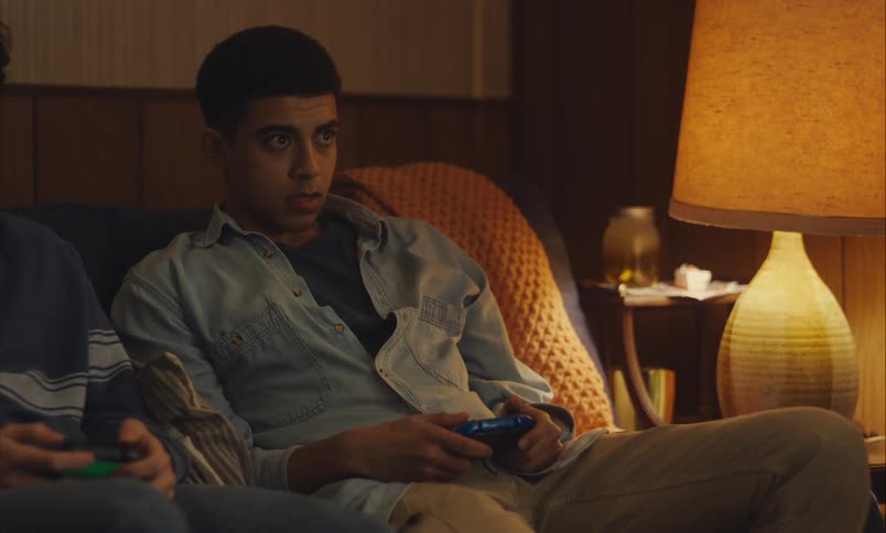 Three diverse teenage friends are engrossed in playing video games together on a couch in a cozy, dimly lit room