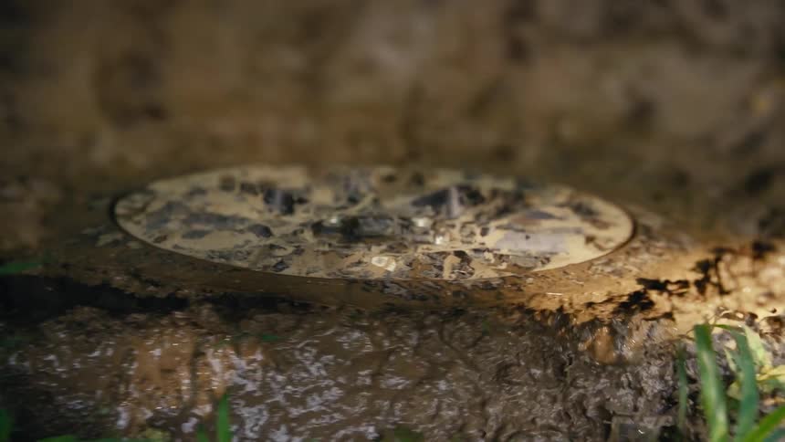A muddy ground light is slowly buried as mud and water flow over it in a gritty close-up