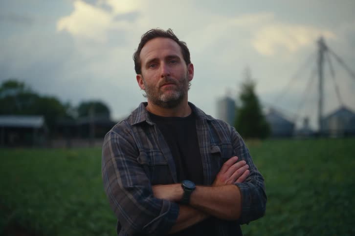 Portrait of a proud and serious farmer standing in a field at dusk with his arms crossed