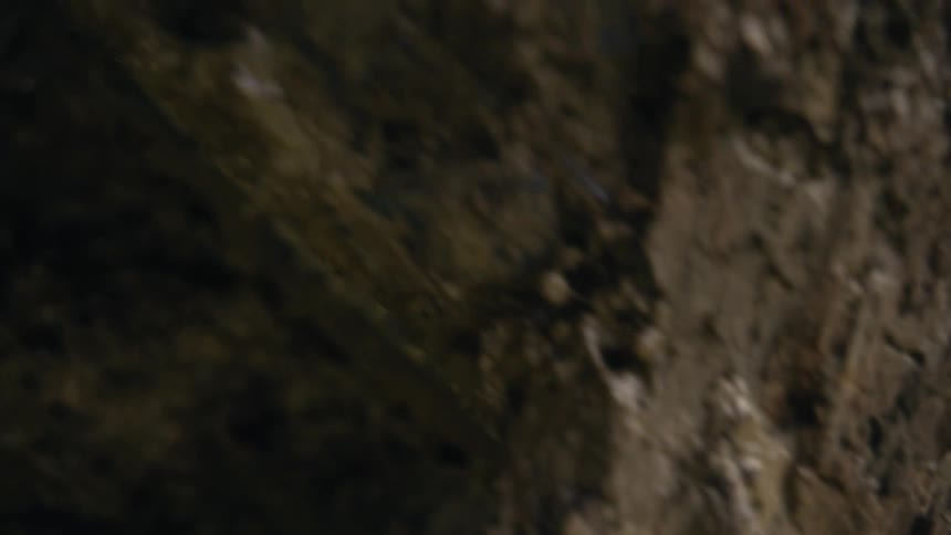 Close up slow motion dolly shot reveals a dark cave's ceiling reflected in a small pool of water on the ground