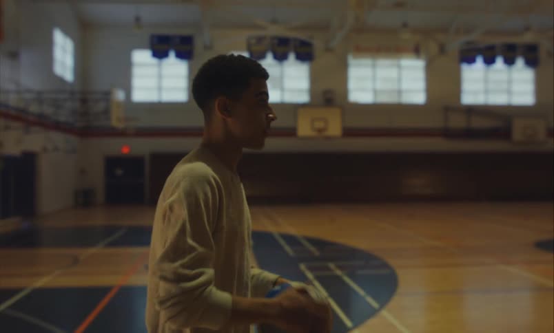 A focused young man practices dribbling and shooting a ball in slow motion on an empty indoor basketball court