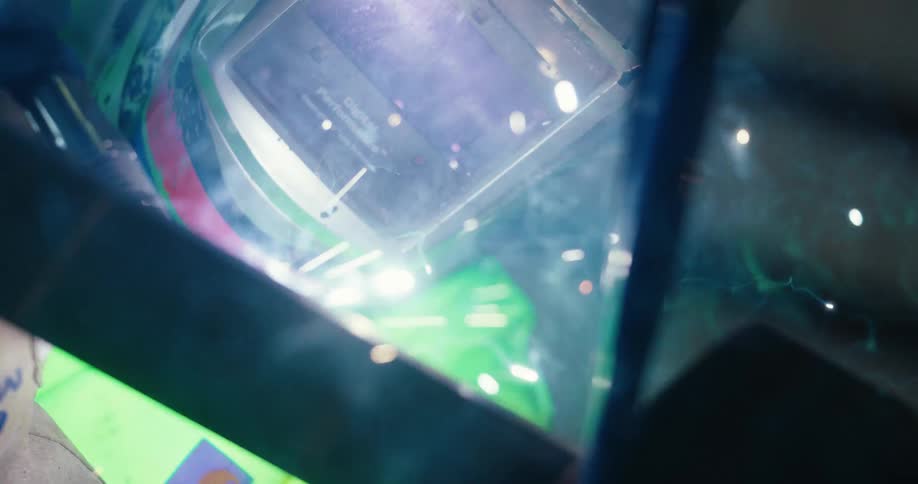 Close-up slow motion footage captures the intense light, smoke, and sparks of welding reflected on a protective helmet