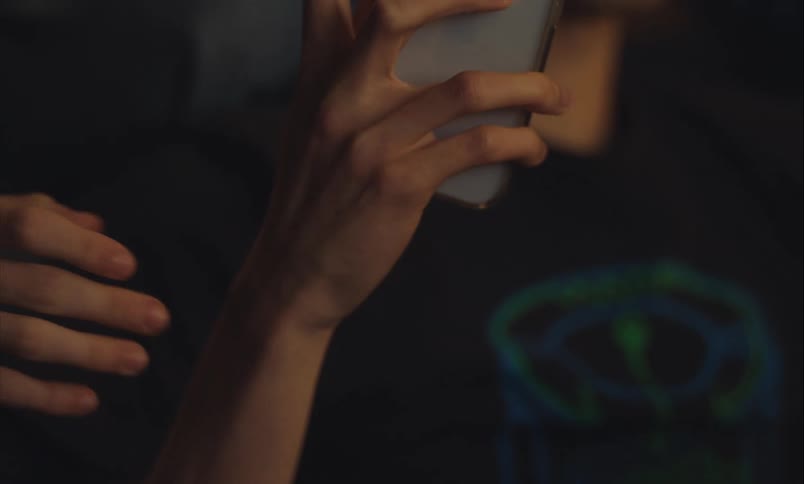 A dramatic close-up of one person's hand grabbing the wrist of another who is holding a smartphone