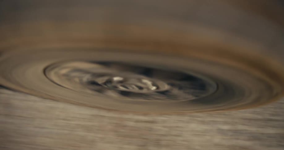A dramatic close-up of a vehicle's dusty tire spinning rapidly while driving off-road on a dirt path