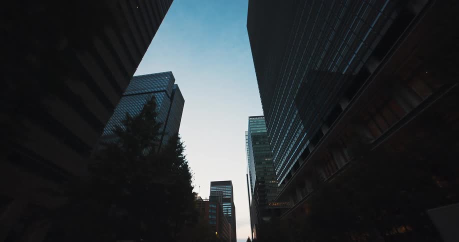 A slow, low-angle dolly shot looking up at modern skyscrapers silhouetted against a serene twilight sky in a downtown financial district