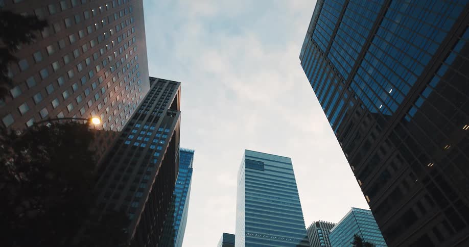 A slow, low-angle dolly shot looks up at towering modern skyscrapers in a city's financial district