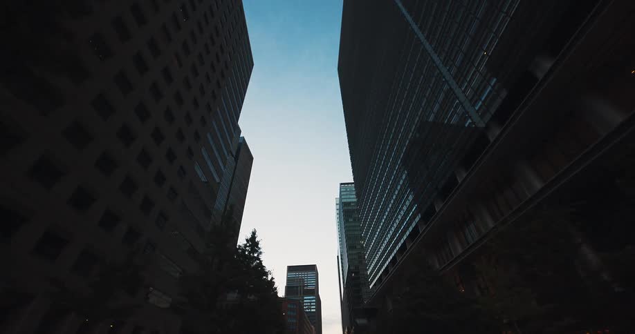 A slow-moving, low-angle shot traveling backward between towering modern skyscrapers at dusk