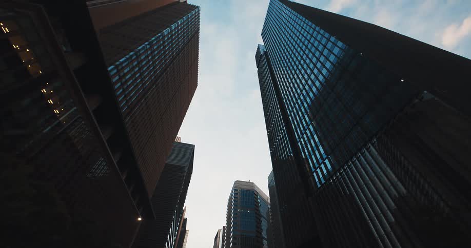 A slow pull-back from a low-angle perspective reveals the towering glass and steel skyscrapers of a modern city against the sky