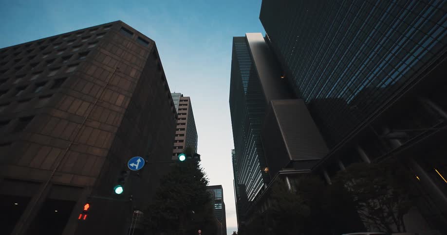 A slow, low-angle point-of-view shot driving through a modern downtown city canyon surrounded by towering skyscrapers