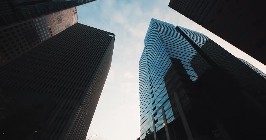 A smooth dolly-out shot from a low angle reveals the towering modern skyscrapers of a bustling city at dusk