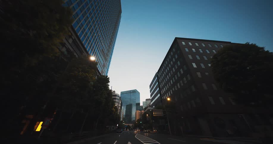 A point-of-view shot slowly driving through a quiet, modern city canyon with towering glass buildings at dawn