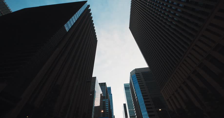 A slow, forward-moving, low-angle shot captures the towering modern skyscrapers of a city's financial district against the sky