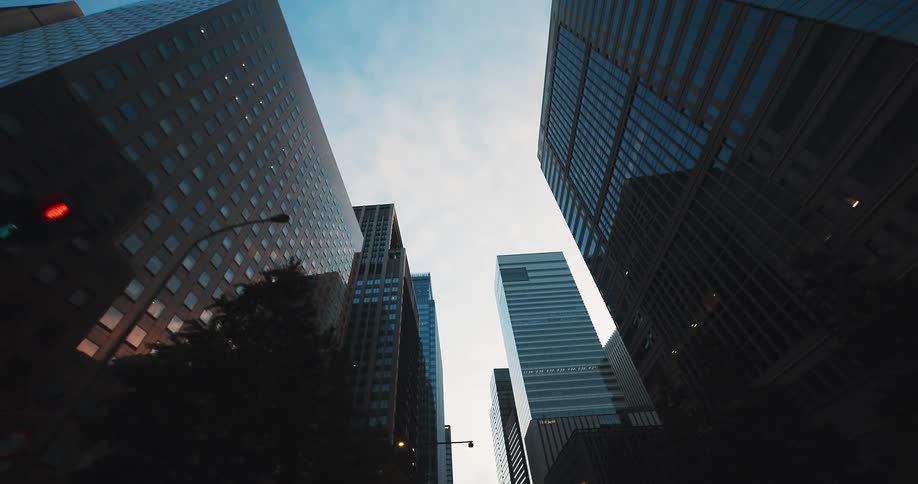 A slow, dramatic pullback shot looking up at towering skyscrapers and the sky in a modern city