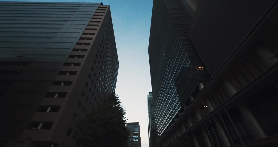 A smooth, low-angle dolly shot glides through a canyon of modern skyscrapers in a quiet metropolitan business district