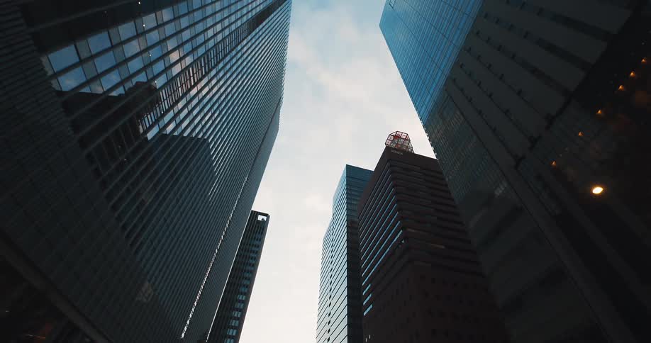 A slow, low-angle tracking shot reveals towering glass skyscrapers in a modern downtown financial district