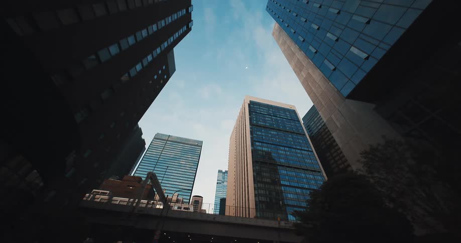 Emerging from a dark city underpass reveals a low-angle view of towering glass skyscrapers against a blue sky
