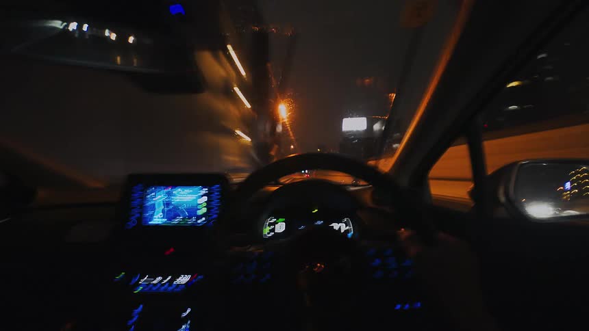 First-person perspective time-lapse of driving through the glowing city streets at night, with lights streaking past