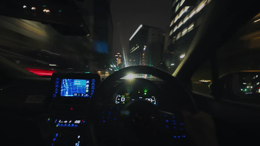 Dynamic first-person view of driving a car through an illuminated city at night, with motion-blurred lights creating a timelapse effect