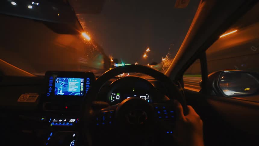 First-person perspective timelapse of driving on a city highway at night in the rain, with illuminated street lights creating a blur of motion