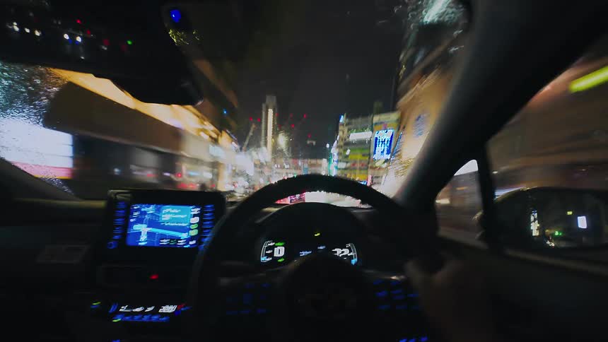 A fast-paced time-lapse from the driver's point of view driving through a rainy, neon-lit city at night