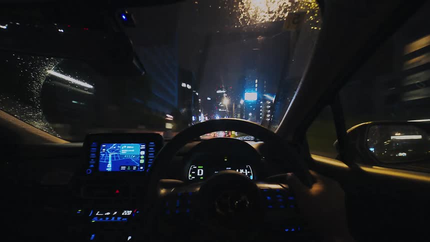 A first-person point-of-view hyper-lapse captures a fast drive through the rainy, neon-lit streets of a modern city at night