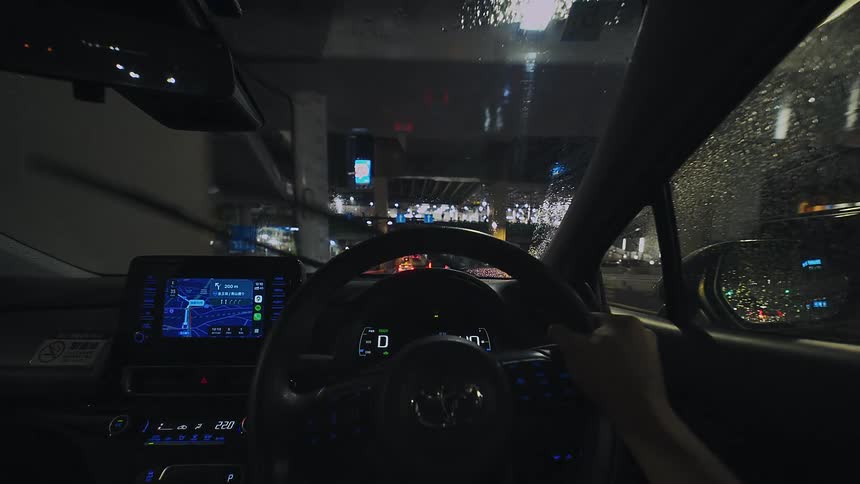 A first-person view of driving through a bustling city on a rainy night, with streetlights reflecting off the wet windshield