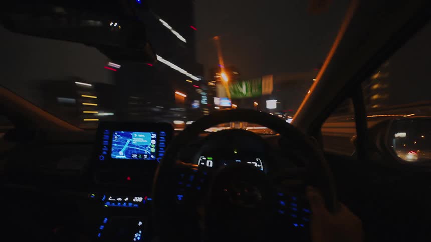 An energetic hyper-lapse from the driver's perspective shows a car speeding through the brightly lit streets of a city at night