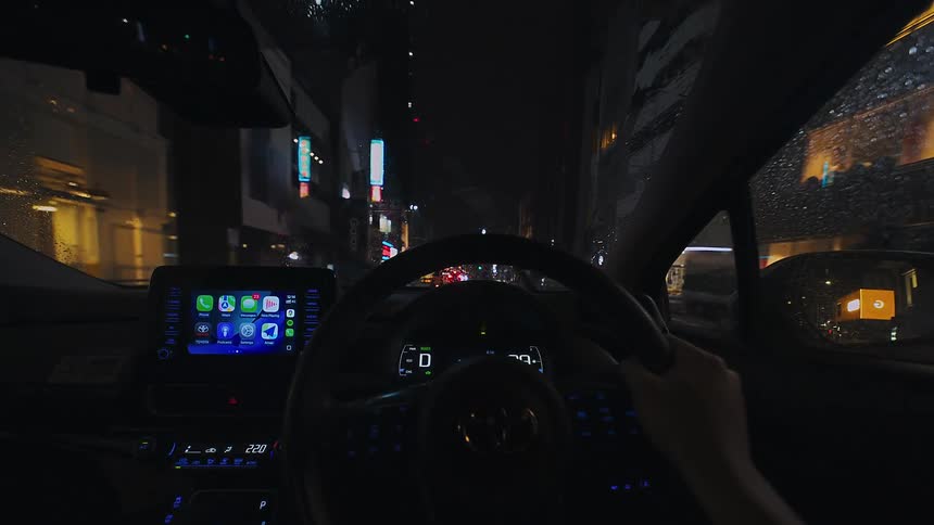 Driver's point of view of a slow drive through the neon-lit streets of a Japanese city on a rainy night