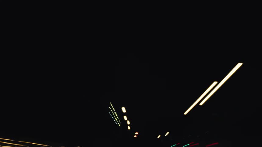 A dizzying hyperlapse captures abstract streaks of colorful city lights from the perspective of a moving car at night