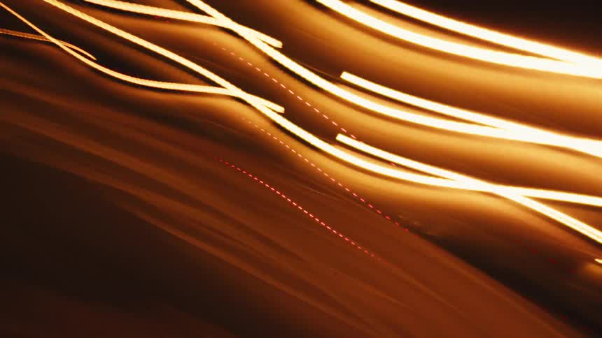Dynamic golden light trails streak and wave across a dark background in an abstract motion blur