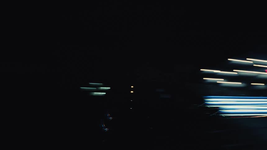 A time-lapse from a moving vehicle captures abstract, colorful streaks of light while driving through a city at night