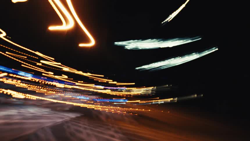 An abstract long-exposure time-lapse of driving through a bustling city at night captures colorful streaks of light in a chaotic blur