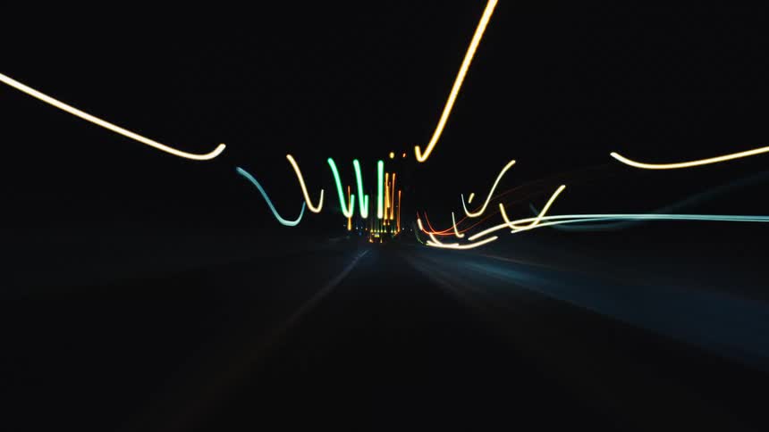 An abstract POV time-lapse of driving at night, with city and tunnel lights creating vibrant, streaking patterns
