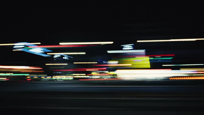 An abstract point-of-view shot of blurred city lights streaking by while driving down a street at night