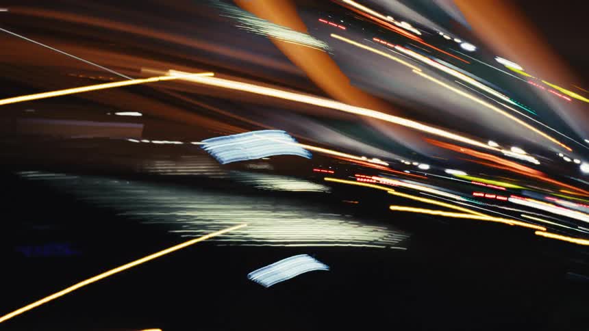 A dynamic and chaotic montage of abstract, colorful light trails streaking across a dark night sky