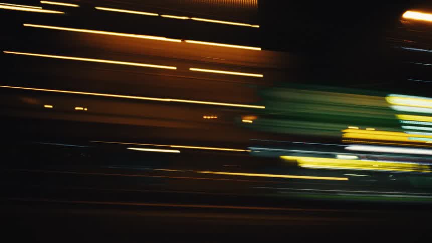 Vibrant, abstract light trails streak across the screen in a fast-paced urban night scene