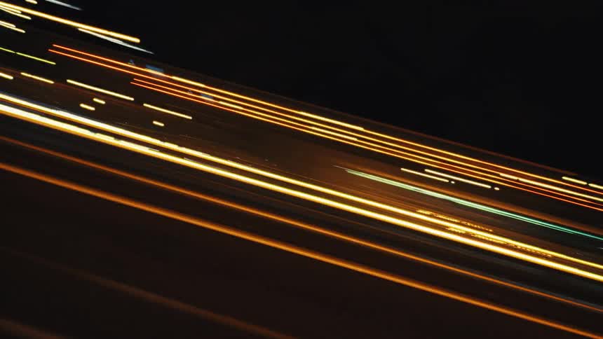 A long exposure time-lapse captures the colorful light trails of cars speeding down a highway at night