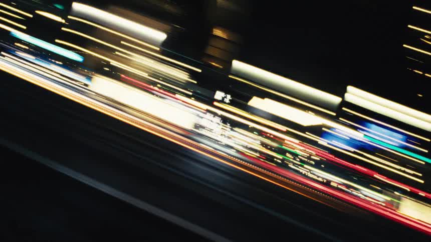 A tilted, high-speed, long-exposure view of urban traffic at night creates abstract streaks of colorful light