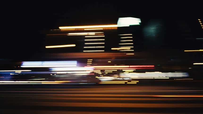 A seamless time-lapse loop of abstract, colorful light streaks from a fast drive through a bustling city at night