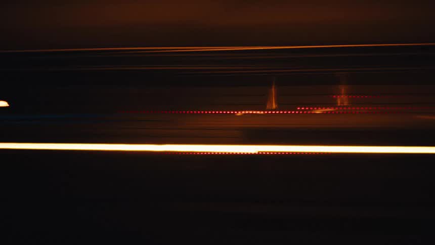 Dynamic abstract light trails of red and orange blur across a dark background at night creating a sense of speed