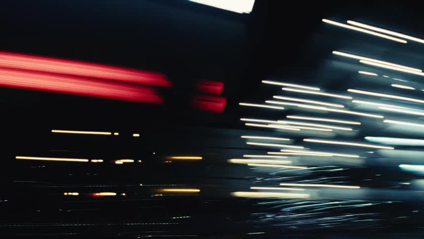 Abstract streaks of colorful city lights blur past during a fast-paced night drive through a tunnel