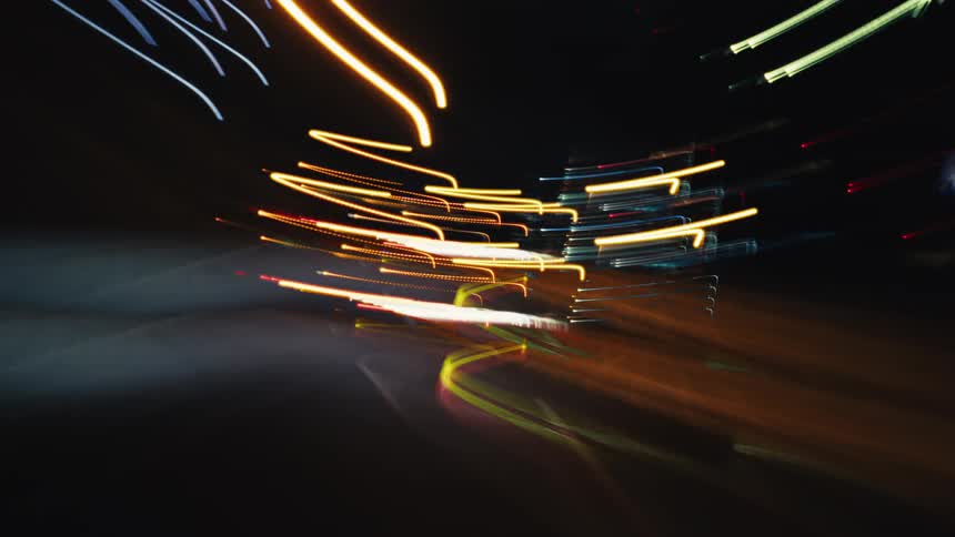 An abstract, high-speed time-lapse captures streaks of vibrant city lights from a driver's perspective at night