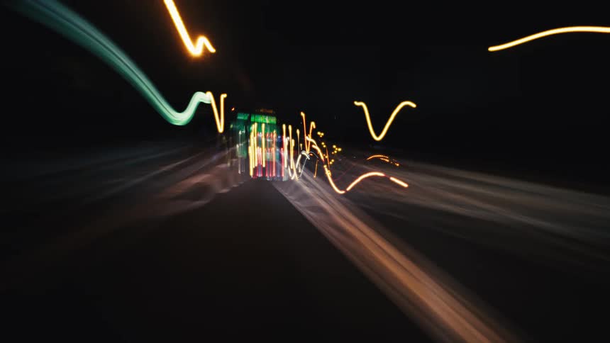 An abstract, long-exposure point-of-view of driving on a dark highway at night, with car lights creating colorful, streaking patterns