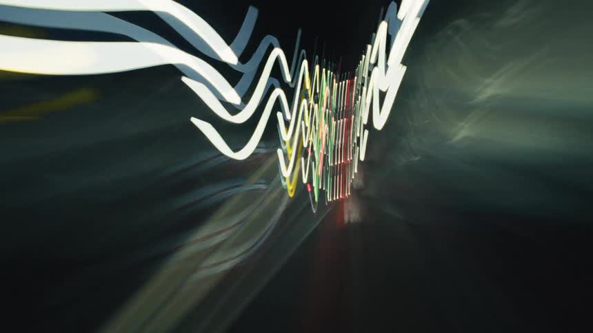A disorienting time-lapse from a moving vehicle captures abstract, colorful streaks of city lights painting the dark night highway