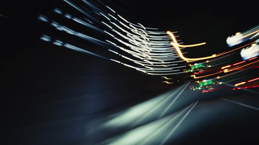 A fast-paced and abstract time-lapse of driving on a highway at night, showing colorful streaks of light from traffic and street lamps