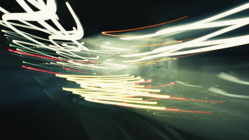 An abstract long-exposure time-lapse captures a frenetic drive through a highway tunnel at night, with vehicle lights creating colorful streaks
