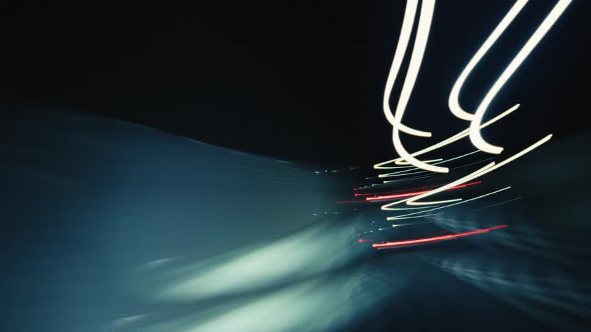 An abstract, long-exposure time-lapse captures streaks of colorful lights while driving through a city at night
